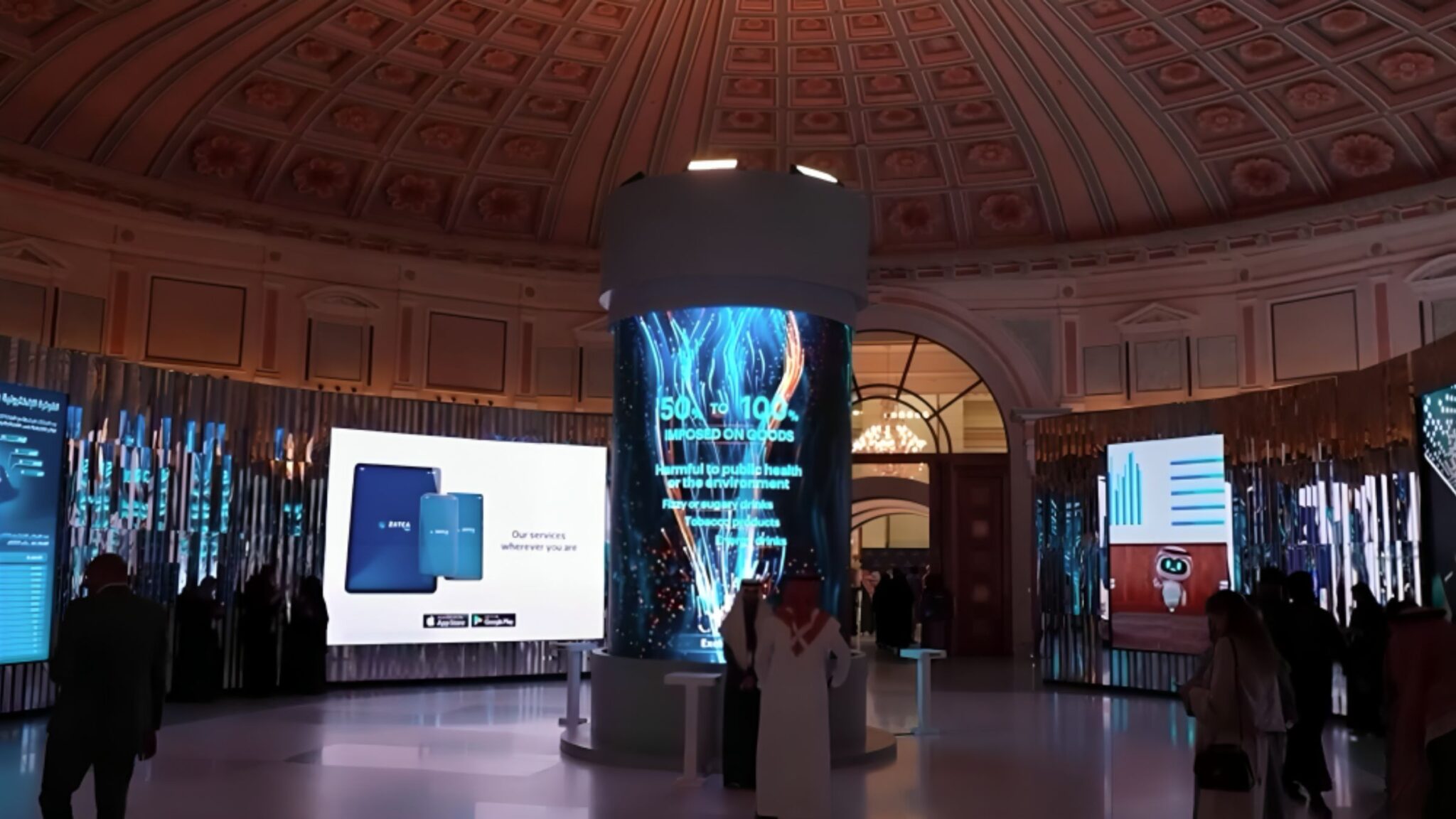 People standing in an exhibition hall with digital displays and a large central column featuring graphics and information. Battle Royal Studios.
