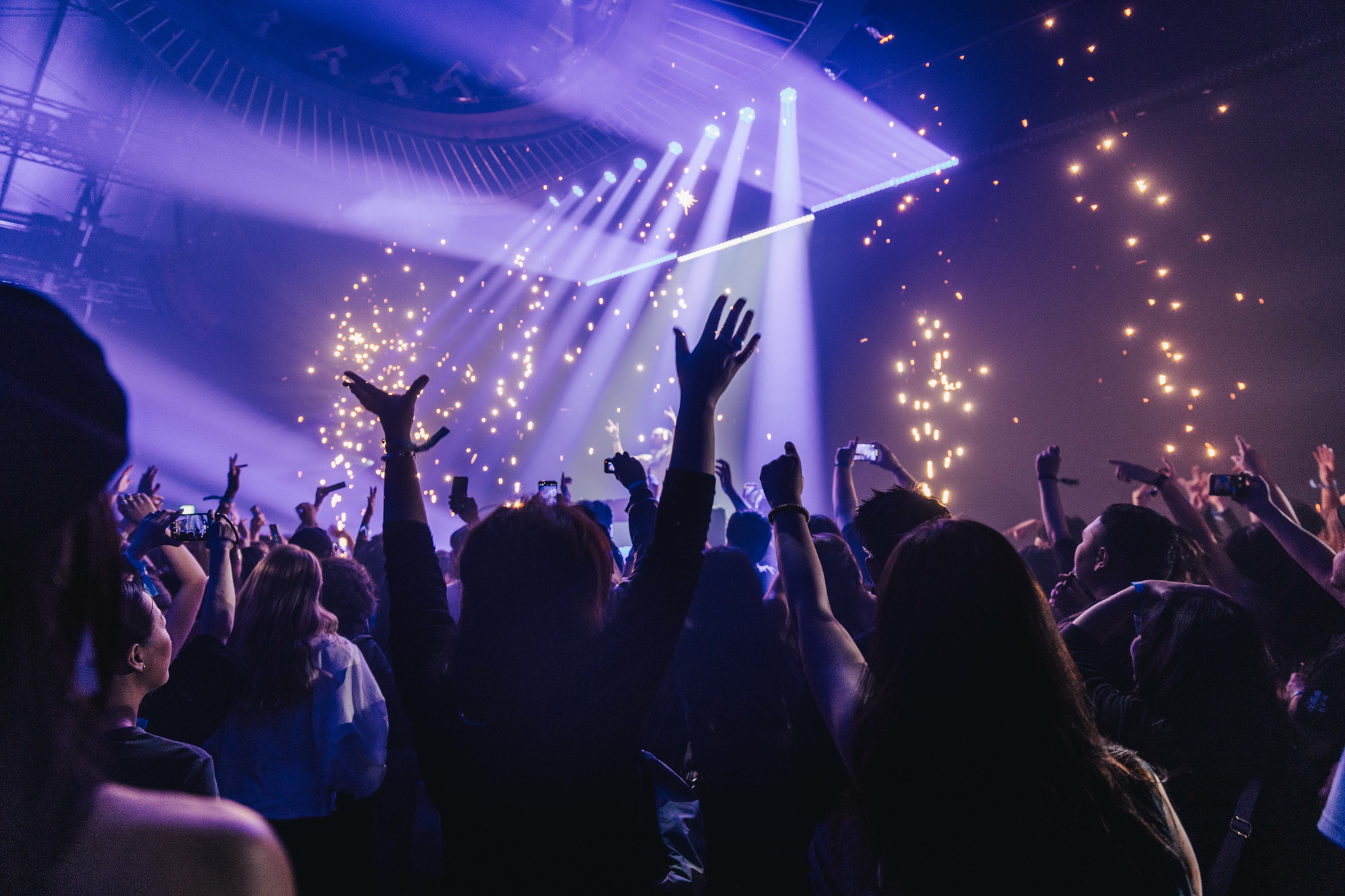 A crowd raises their hands and captures the moment on their phones as stage lights and sparks illuminate a live performance Battle Royal Studios