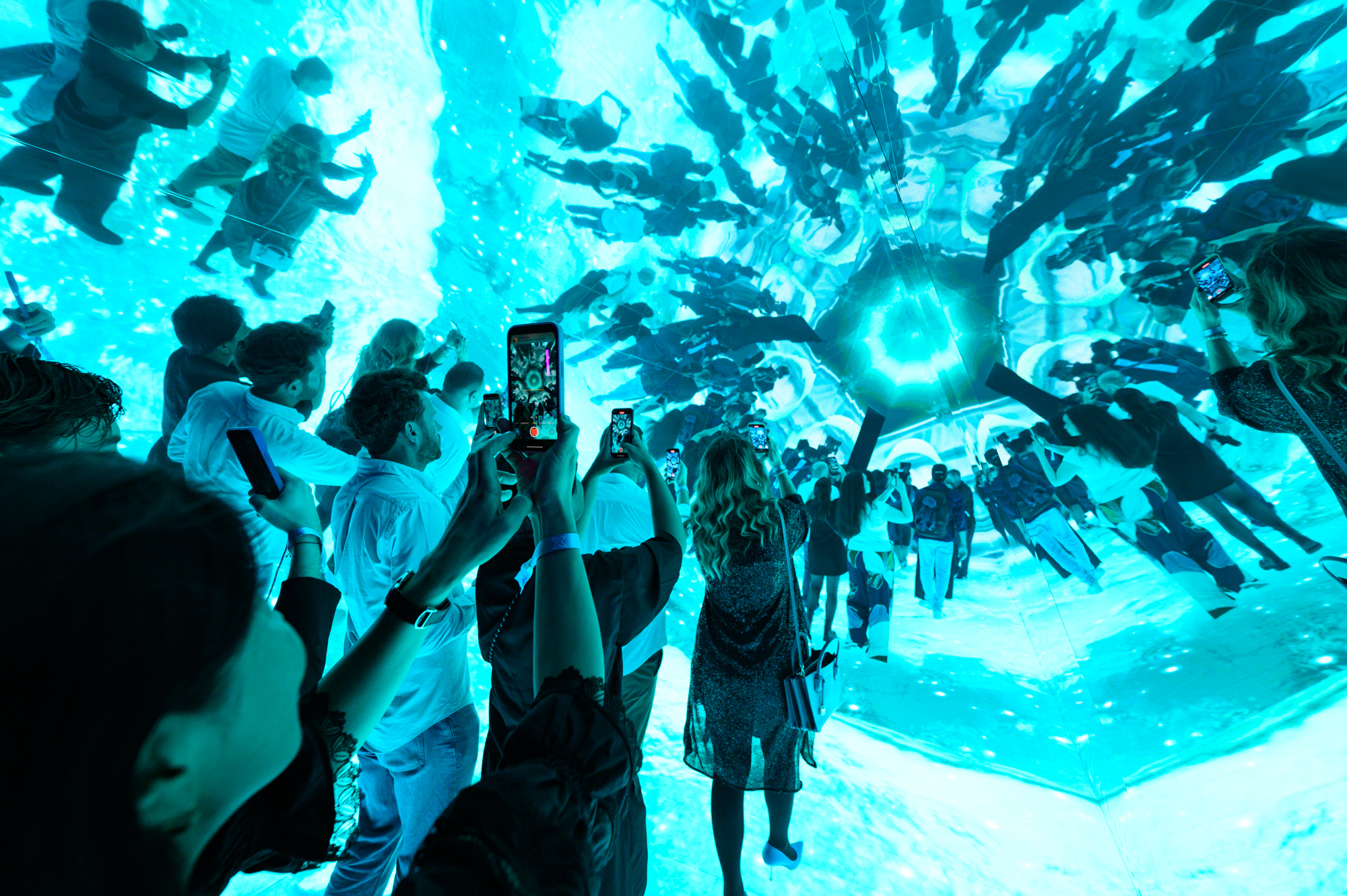 Crowd inside an immersive digital art installation with mirrored reflections and vibrant blue lighting, capturing the moment on their smartphones Battle Royal Studios